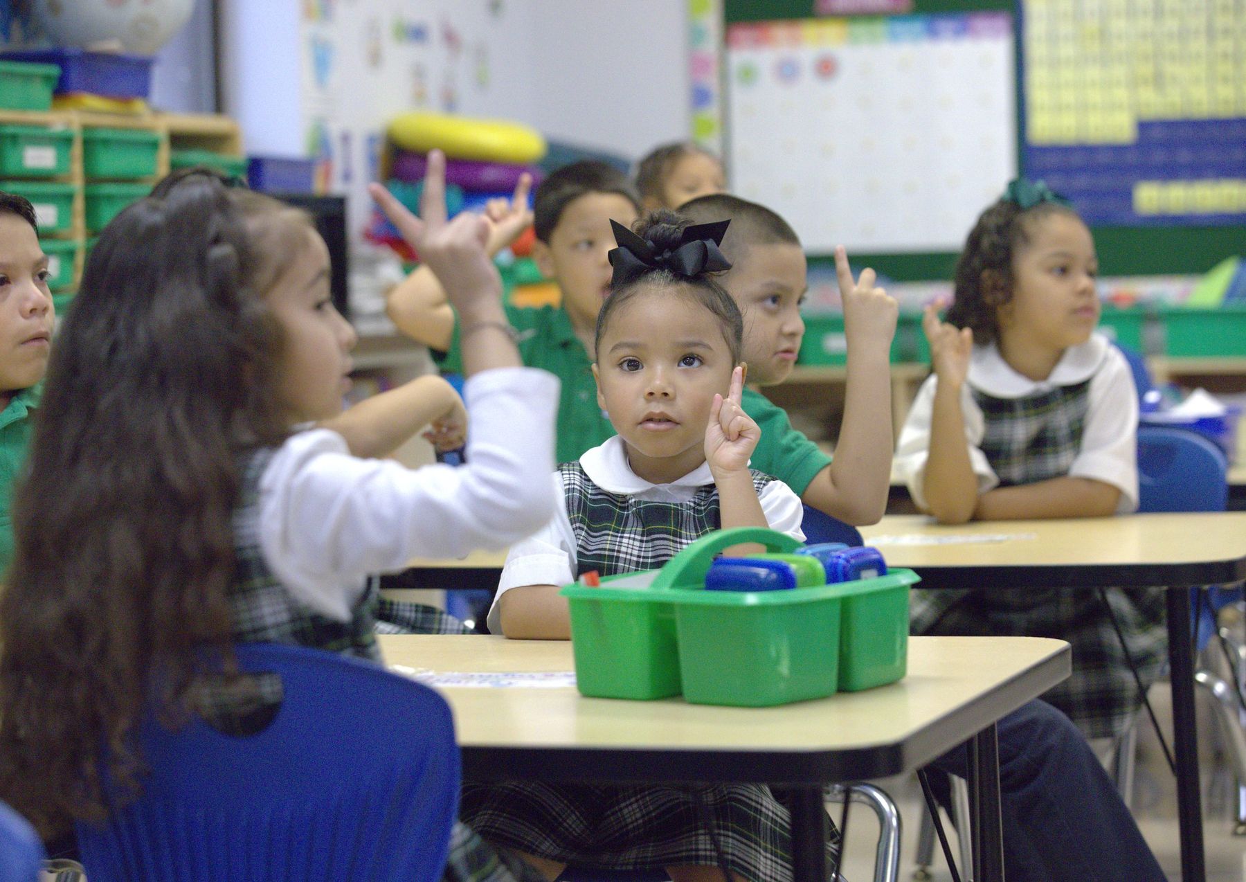 Young Compass students raising their hands in class
