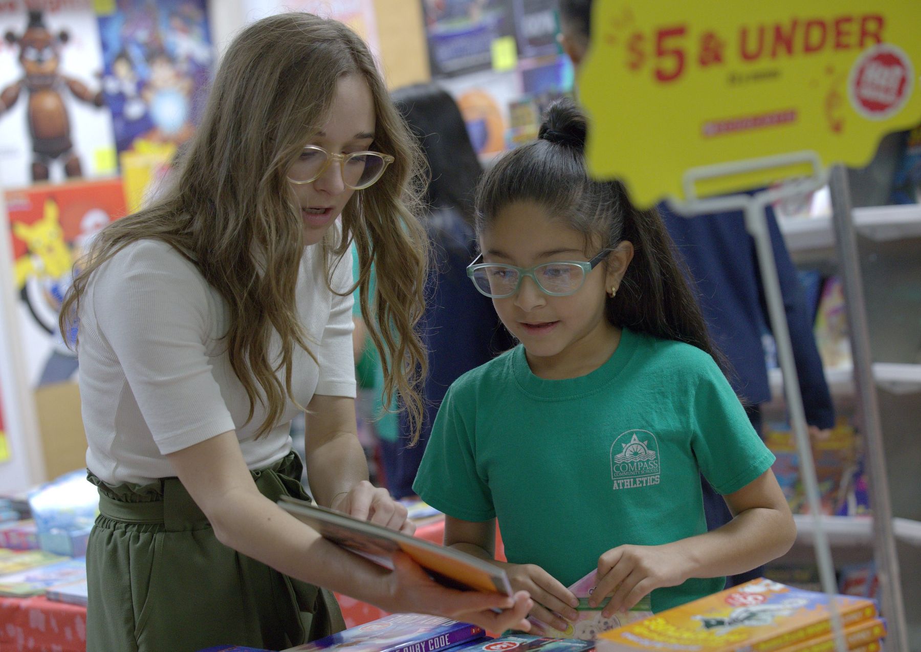 Compass teacher helping a student choose a book at the book fair